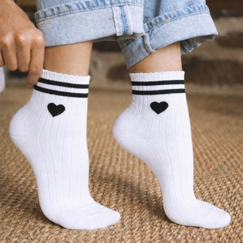 Chaussettes EVJF blanches avec coeur noir et rayures noires, portees avec un jean, accessoire tendance pour enterrement de vie de jeune fille.