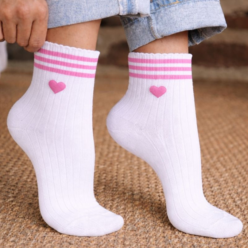 Chaussettes EVJF blanches avec coeur rose et rayures roses, portees avec un jean, accessoire pour enterrement de vie de jeune fille.