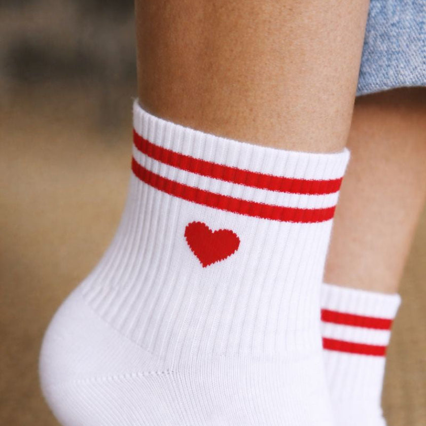 Gros plan sur des chaussettes EVJF blanches avec cœur rouge et rayures rouges, accessoire original pour enterrement de vie de jeune fille.
