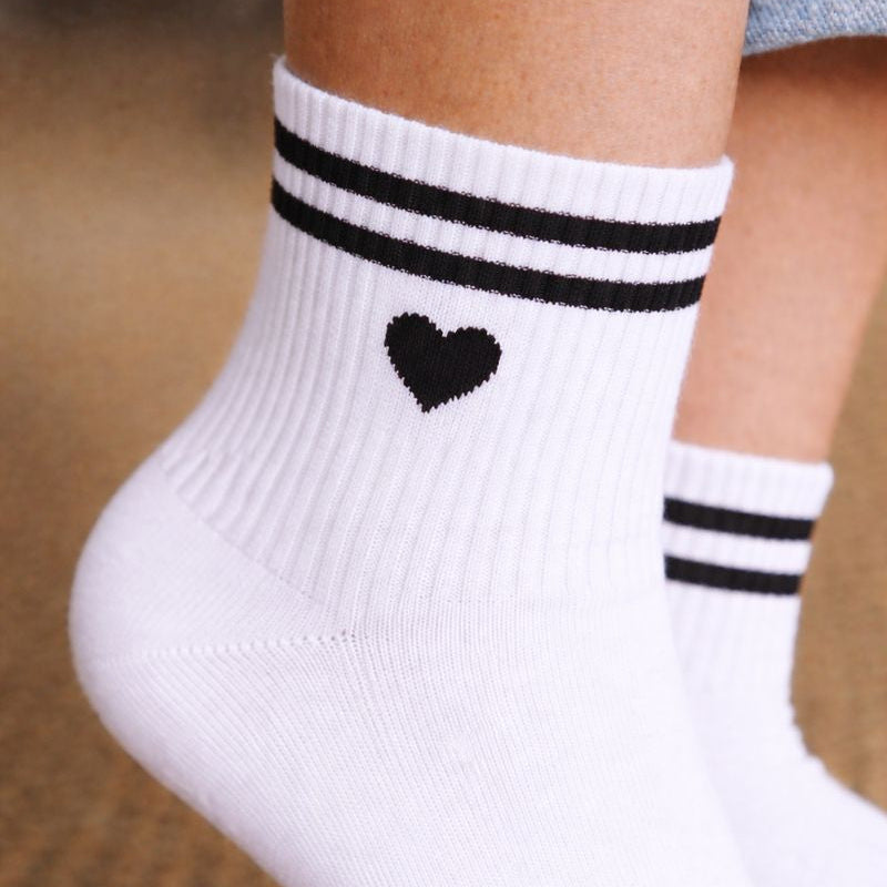 Gros plan sur des chaussettes EVJF blanches avec coeur noir et rayures noires, accessoire tendance pour enterrement de vie de jeune fille.
