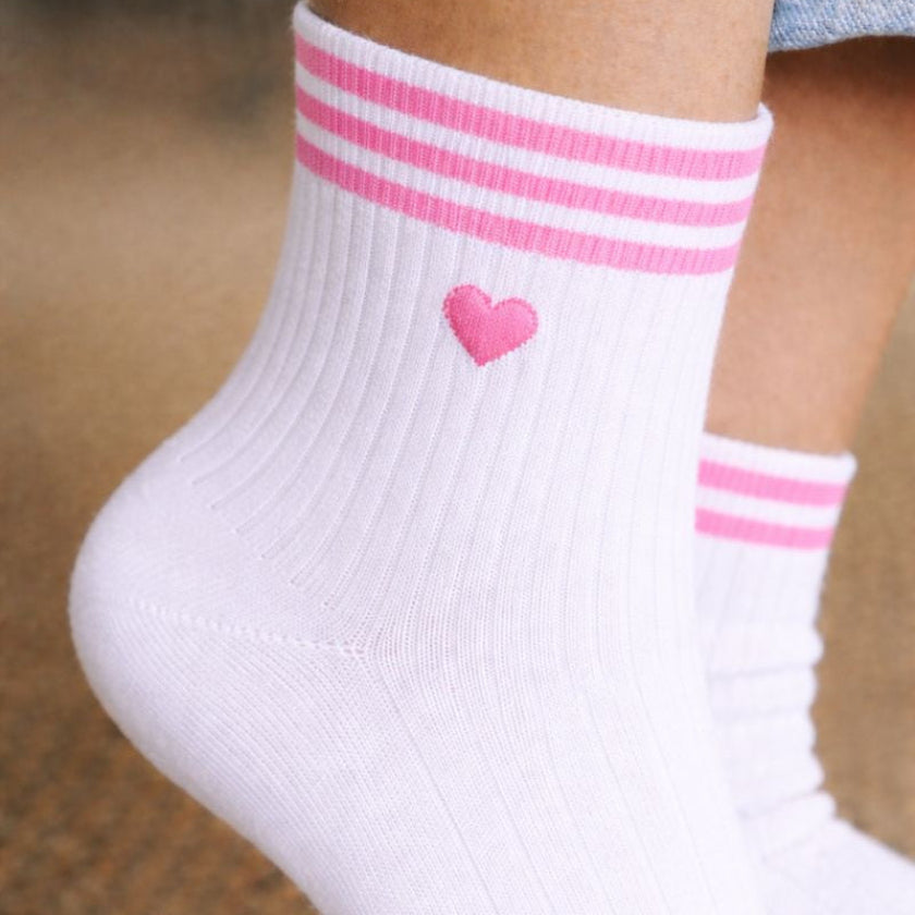 Gros plan sur des chaussettes EVJF blanches avec motif coeur rose et rayures roses, accessoire pour enterrement de vie de jeune fille.