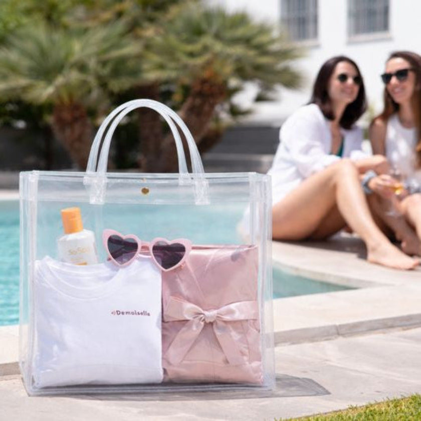 Coffret evjf demoiselle avec sac transparent contenant tee shirt lunettes coeur accessoires au bord de la piscine
