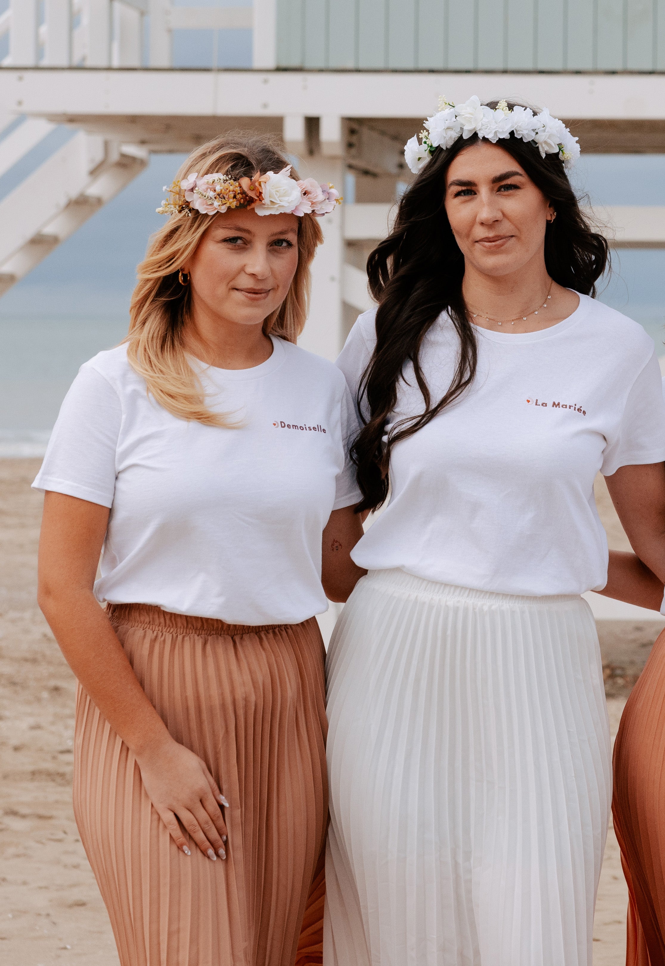 Future mariee et demoiselle portant des couronnes de fleurs EVJF, tenues blanches et jupes plissees pour celebration en bord de mer.