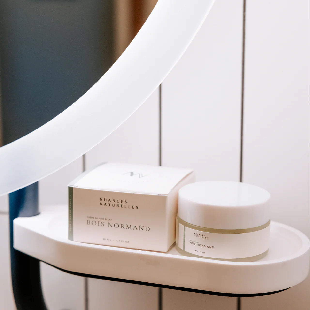 Crème visage naturelle ‘Bois Normand’ de Nuances Naturelles, présentée sur une étagère de salle de bain blanche avec miroir, soin beauté élégant à offrir lors d’un EVJF.
