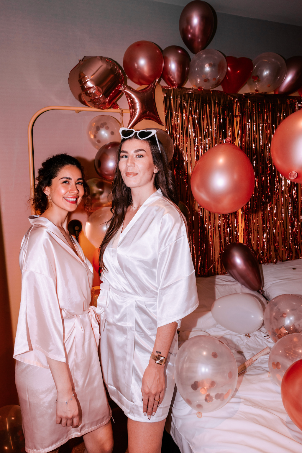 Amies posant lors dun EVJF avec peignoirs satin et decoration de ballons rose gold, ambiance festive et elegante.