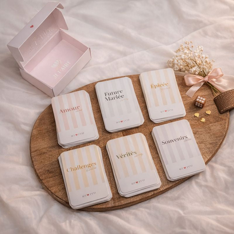 Jeu de cartes EVJF MyEVJF posé sur un plateau en bois : cartes ‘Amour’, ‘Future Mariée’, ‘Épicée’, ‘Souvenirs’, ‘Vérités’ et ‘Challenges’, présenté dans un coffret rose élégant pour enterrement de vie de jeune fille.