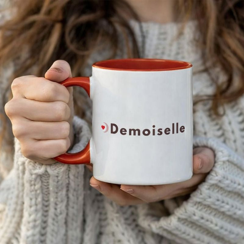 Mug EVJF blanc avec interieur et anse rouges inscription demoiselle tenu en main par une femme en pull.
