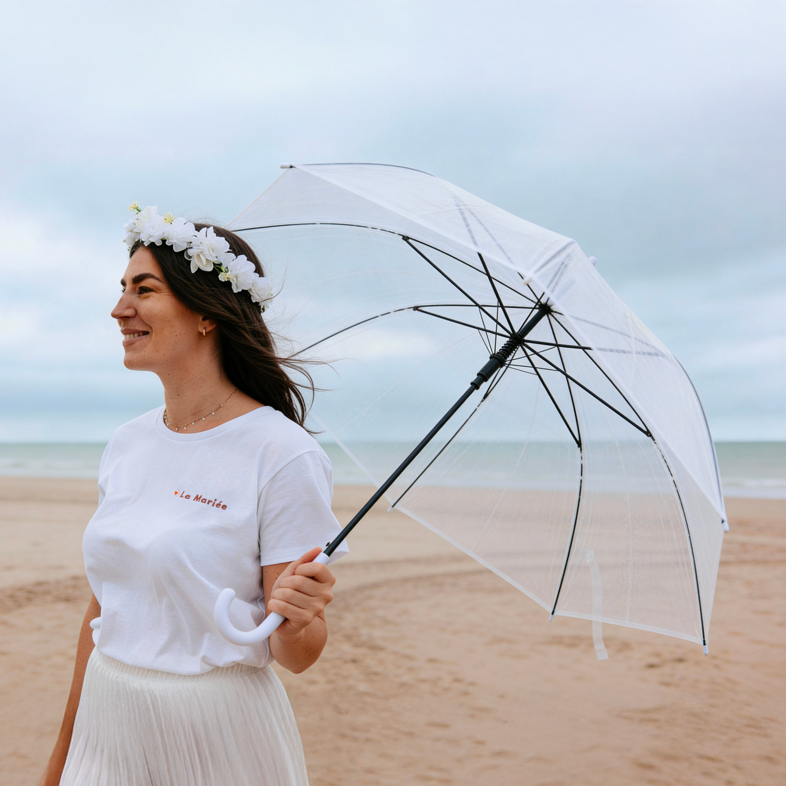 Future mariee portant un parapluie transparent EVJF a la plage, accessoire elegant pour une seance photo enterrement de vie de jeune fille.