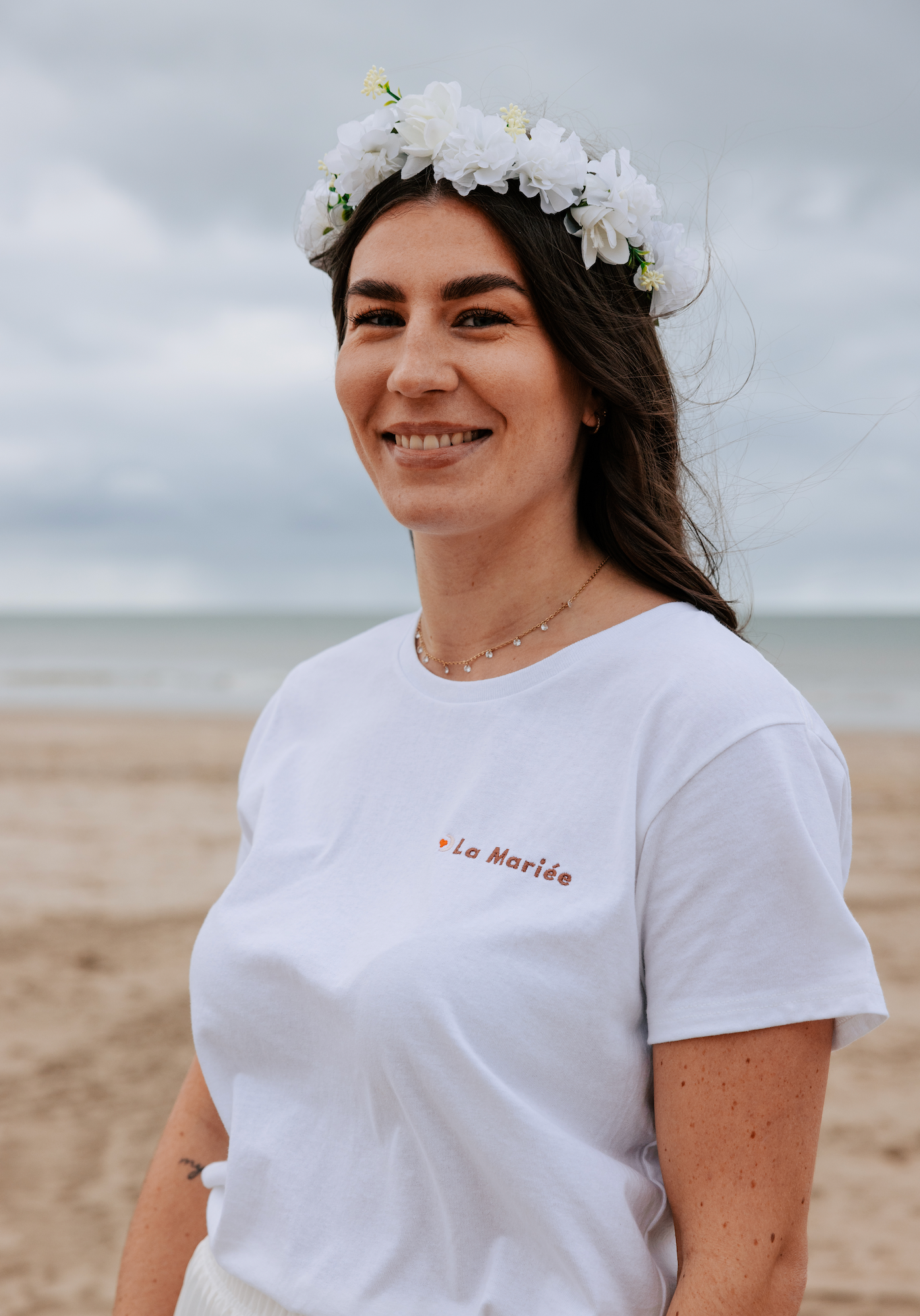 Femme portant t shirt EVJF blanc la mariee avec couronne de fleurs sur la plage