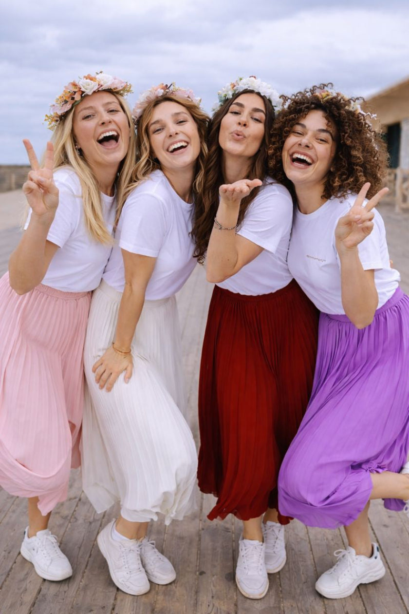 Groupe de femmes celebrant un EVJF en portant des jupes plissees colorees et des t shirts blancs, ambiance festive et joyeuse.