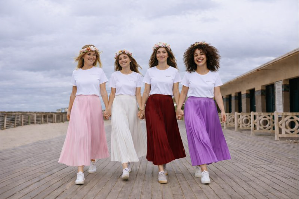 Groupe damies marchant main dans la main lors dun EVJF, portant des jupes plissees longues et des t shirts blancs assortis.