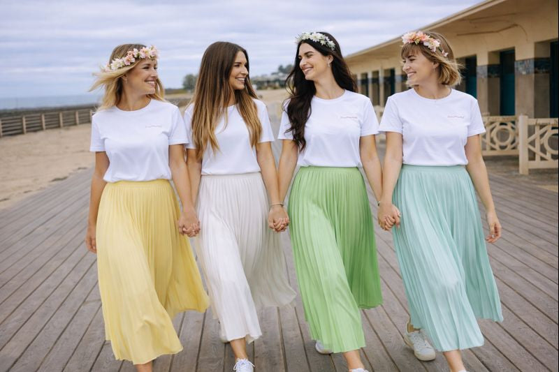 Groupe damies se tenant la main lors dun EVJF, portant des jupes plissees pastel longues et des t shirts blancs assortis.